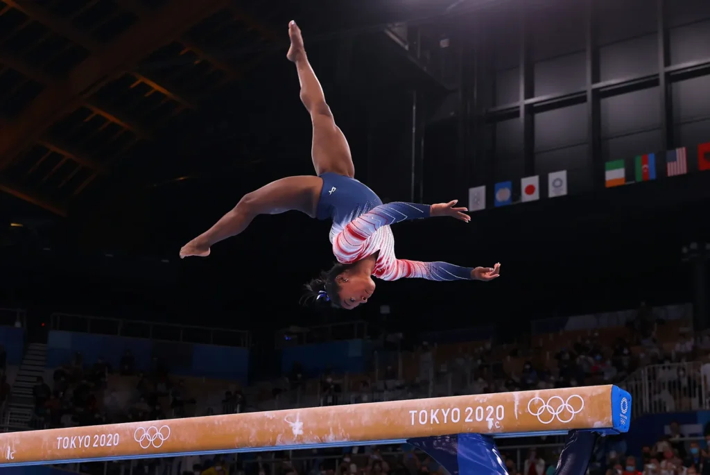 Simone Biles in the air while performing on a balance beam for USA Gymnastics